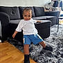 black_sneakers, blue_shorts, casual_clothing, child, couch, cozy, floor, furniture, happy, home, indoor, living_room, person, playful, rug, smiling, toddler, white_tshirt, wooden_floor, young_child