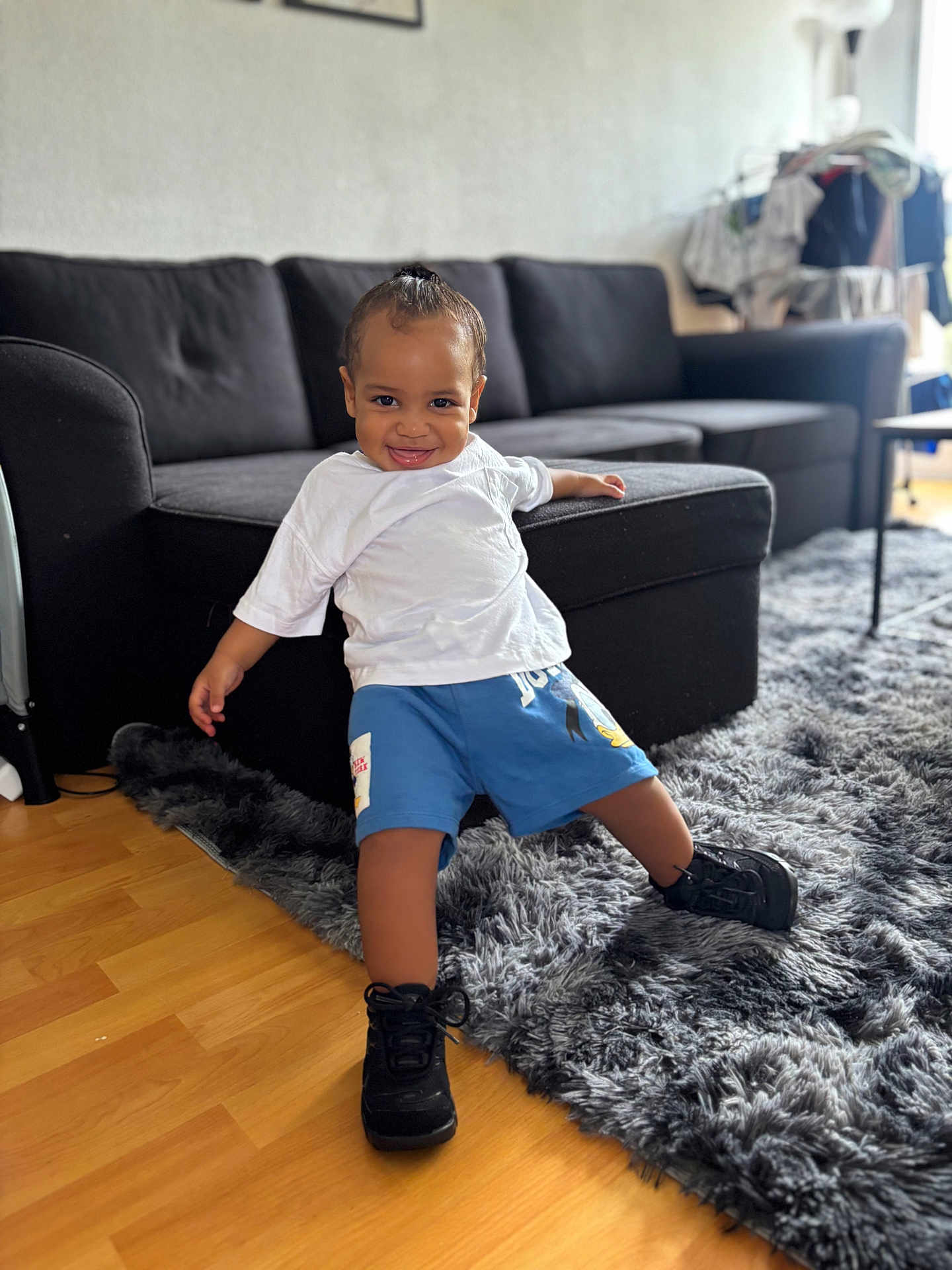 Kessim participe au concours pour gagner de l'argent avec cette photo : black_sneakers, blue_shorts, casual_clothing, child, couch, cozy, floor, furniture, happy, home, indoor, living_room, person, playful, rug, smiling, toddler, white_tshirt, wooden_floor, young_child