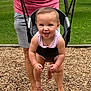 toddler, child, swing, playground, grass, woodchips, adult, smiling, outdoor, summer, fun, joyful, person, feet, legs, clothing, park, daytime, happy, recreation