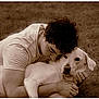man, dog, grass, outdoor, pet, animal, friendship, affection, curly_hair, white_dog, casual_clothing, embrace, love, relaxation, portrait, nature, companionship, lying_down, sepia_tone, calm