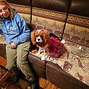 Laylah is registered to the contest to win money with this photo: bows, brown_leather, carpet, casual_clothing, couch, cozy, dog, floor, furniture, glasses, home, indoor, looking_at_camera, patterned_blanket, pet, red_dress, rustic_decor, sitting, woman, wood_paneling