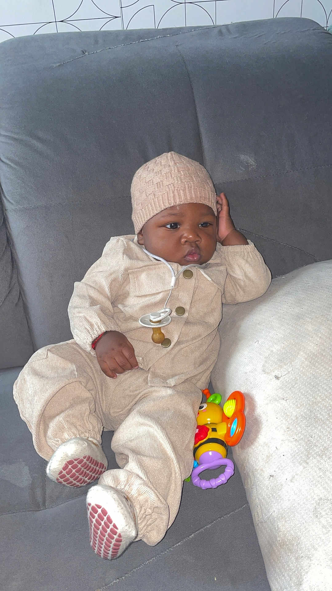 Emerys participe au concours pour gagner de l'argent avec cette photo : baby, infant, child, couch, gray_couch, beige_clothing, knit_hat, pacifier, toy, colorful_toy, sitting, indoor, relaxed, cute, young_child, footwear, plush_couch, portrait, casual, cozy