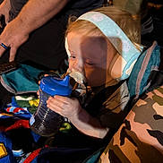 Hunter is registered to the contest to win money with this photo: toddler, child, headphones, sippy_cup, stroller, blanket, camouflage, hand, arm, shadow, blue, clothing, person, baby, drinking, seatbelt, outdoor, fabric, closeup, portrait