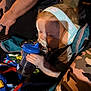 toddler, child, headphones, sippy_cup, stroller, blanket, camouflage, hand, arm, shadow, blue, clothing, person, baby, drinking, seatbelt, outdoor, fabric, closeup, portrait