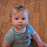 Rowan is registered to the contest to win money with this photo: baby, child, floor, wooden_floor, curly_hair, striped_shirt, blue_shirt, bear_graphic, sitting, indoor, cute, young_child, portrait, looking_at_camera, casual_clothing, short_sleeves, infant, person, human, light_brown_hair