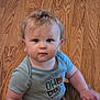 baby, bear_graphic, blue_shirt, casual_clothing, child, curly_hair, cute, floor, human, indoor, infant, light_brown_hair, looking_at_camera, person, portrait, short_sleeves, sitting, striped_shirt, wooden_floor, young_child