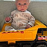 baby, child, toy, truck, yellow, pajamas, indoor, furniture, blanket, face, expression, cute, sitting, vehicle, wheel, floor, young, infant, play, serious