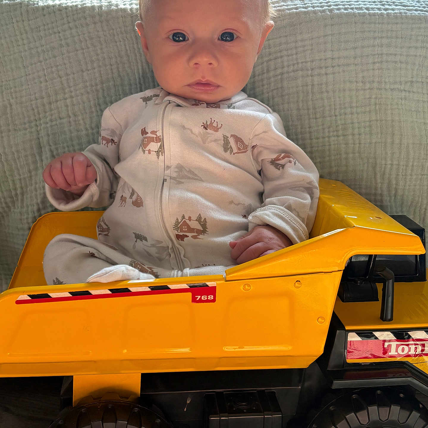 Robert is registered to the contest to win money with this photo: baby, child, toy, truck, yellow, pajamas, indoor, furniture, blanket, face, expression, cute, sitting, vehicle, wheel, floor, young, infant, play, serious