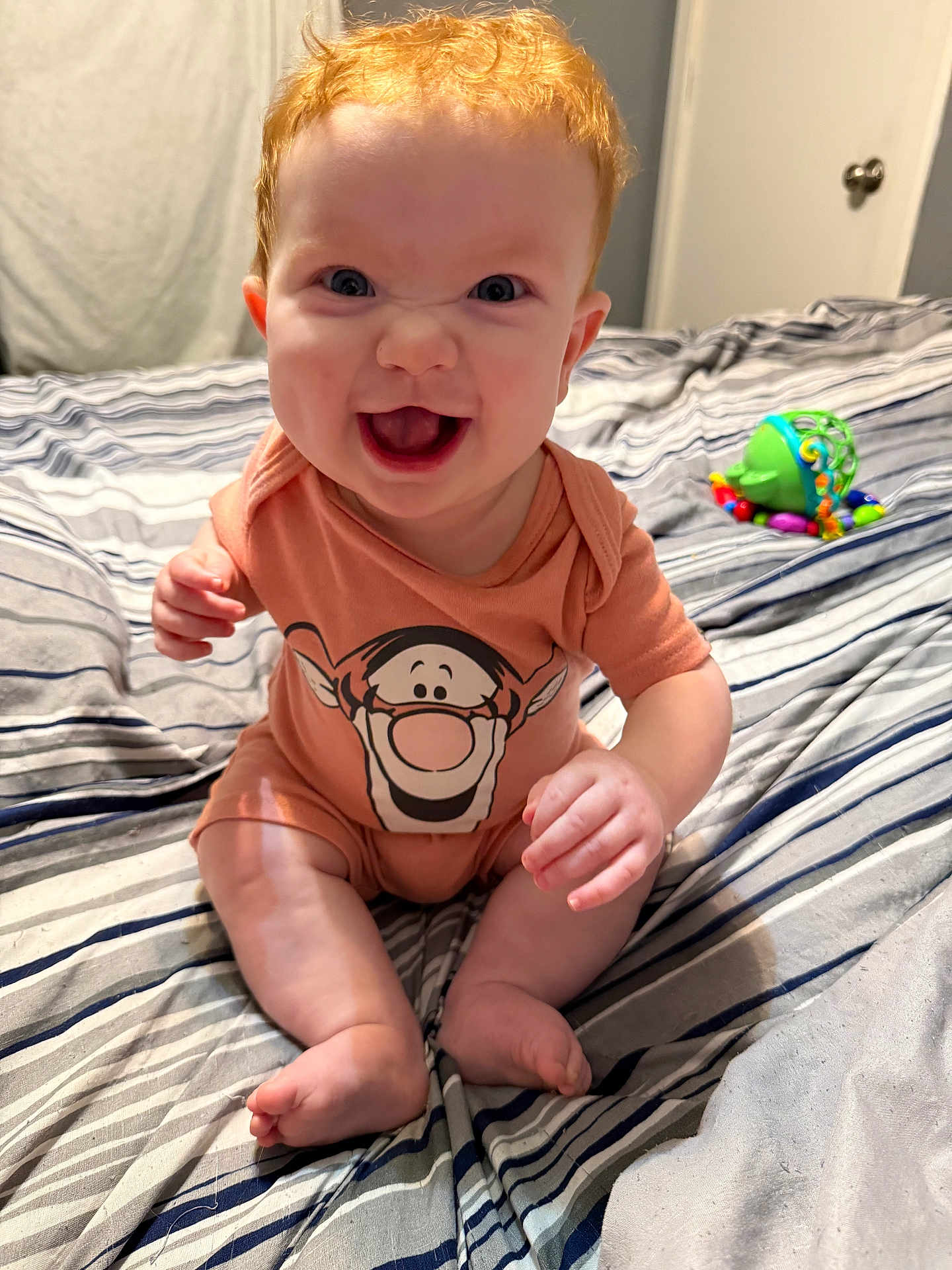 Onyx joined the competition — help win amazing prizes! baby, red_hair, smiling, onesie, cartoon_print, bed, striped_bedspread, toy, indoor, child, happy, sitting, person, infant, cute, barefoot, cheerful, skin, hand, face