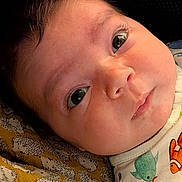 évelyne joined the competition — help win amazing prizes! baby, close_up, face, eyes, infant, child, patterned_blanket, yellow, clothing, fish_print, cute, portrait, skin, expression, lying_down, young_child, indoors, soft_light, head, curious