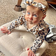 Eloise is registered to the contest to win money with this photo: baby, infant, child, crawling, leopard_print, headband, pajamas, cushion, carpet, wooden_furniture, indoor, curious, wide_eyes, cute, person, portrait, hands, face, expression, soft_lighting