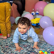 Aëlan participe au concours pour gagner de l'argent avec cette photo : toddler, child, crawling, balloons, toys, carpet, indoor, party, colorful, person, clothing, floor, baby, curly_hair, smiling, hands, feet, background, blurred, sitting