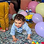 toddler, child, crawling, balloons, toys, carpet, indoor, party, colorful, person, clothing, floor, baby, curly_hair, smiling, hands, feet, background, blurred, sitting