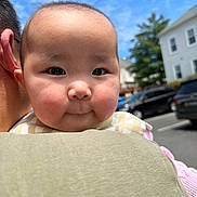 Celine is registered to the contest to win money with this photo: adult, baby, blue_sky, cheeks, child, clothing, cute, daylight, expression, face, happy, head, holding, infant, outdoor, parked_cars, person, portrait, shoulder, sky