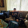 child, boy, couch, pillow, living_room, window, blinds, indoors, sitting, portrait, gift_bag, present, fish_tank, aquarium, stuffed_toy, blanket, clutter, furniture, casual, home