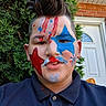 child, boy, face_paint, selfie, portrait, outdoor, garden, hedge, front_door, brick_wall, blue_paint, red_paint, star, patriotic, short_hair, smiling, shirt, close_up, person, daylight