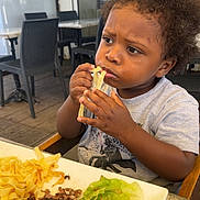 Silas a rejoint le concours — aidez-le/la à gagner de superbes lots ! chair, child, clothing, contemplative, curly_hair, daylight, eating, food, meal, meat, outdoor, pasta, person, plate, portrait, restaurant, salad, table, toddler, window