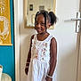 child, girl, smile, dress, white_dress, bracelet, indoor, mirror, door, hairstyle, curly_hair, pigtails, tapestry, table, basket, wall, portrait, happy, standing, room