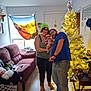 Nico is registered to the contest to win money with this photo: baby, woman, man, christmas_tree, indoor, family, holiday, glasses, beanie, couch, floor, lamp, table, window, decorations, clothing, wood_floor, smile, home, people