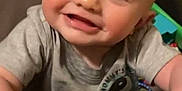 Cooper is registered to the contest to win money with this photo: baby, smiling, child, face, hands, gray_shirt, indoor, toy, cute, young, happy, person, infant, playful, closeup, head, skin, expression, bright_eyes, casual_clothing