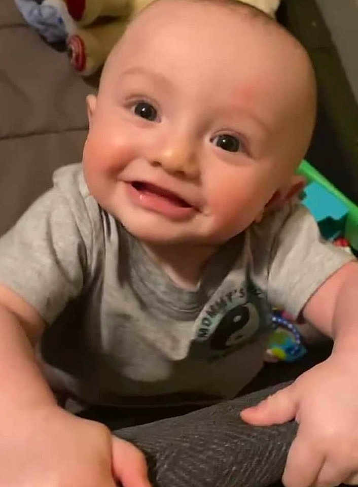 Cooper is registered to the contest to win money with this photo: baby, smiling, child, face, hands, gray_shirt, indoor, toy, cute, young, happy, person, infant, playful, closeup, head, skin, expression, bright_eyes, casual_clothing