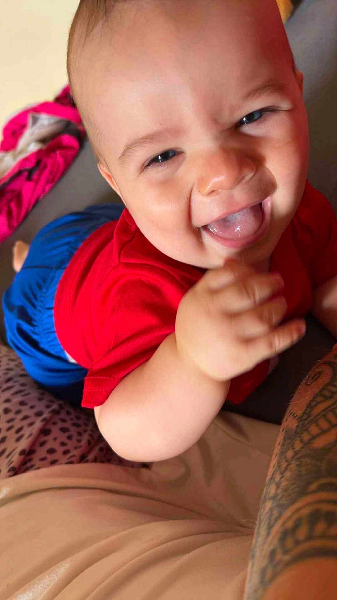 Lisandro a rejoint le concours — aidez-le/la à gagner de superbes lots ! baby, child, smiling, tongue_out, red_shirt, blue_shorts, crawling, tattoo, arm, indoor, happy, skin, face, hand, person, closeup, cute, infant, expression, playful