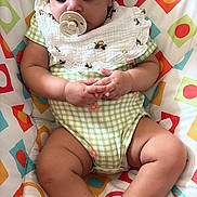 Nora is registered to the contest to win money with this photo: baby, bib, child, clothing, colorful, cute, green, hands, indoors, infant, legs, orange, pacifier, patterned_cushion, peaceful, red, resting, sleeping, soft_lighting, white