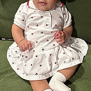 Nora joined the competition — help win amazing prizes! baby, child, infant, dress, headband, bow, socks, couch, green_couch, seated, indoors, cute, smiling, looking_at_camera, white_clothing, patterned_clothing, portrait, young_child, comfortable, corduroy