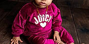 Karma is registered to the contest to win money with this photo: child, toddler, portrait, sitting, velvet_sweatshirt, pink_clothing, curly_hair, barefoot, necklace, heart_logo, wooden_floor, studio_lighting, expressive_eyes, dark_background, cute, indoor, fashion, young_child, face, floor