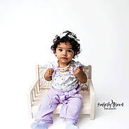 Karma is registered to the contest to win money with this photo: adorable, baby, big_eyes, child, curly_hair, cute, hands, headband, looking_at_camera, mini_bench, necklace, photography, portrait, props, purple_outfit, sitting, studio, toddler, watermark, white_background