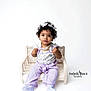baby, toddler, child, curly_hair, headband, necklace, purple_outfit, mini_bench, studio, white_background, portrait, sitting, looking_at_camera, cute, adorable, hands, big_eyes, photography, watermark, props