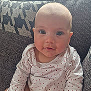 Sophia is registered to the contest to win money with this photo: baby, infant, face, eyes, clothing, shirt, heart_pattern, couch, fabric, texture, person, child, cute, portrait, sitting, indoors, skin, head, happy, young