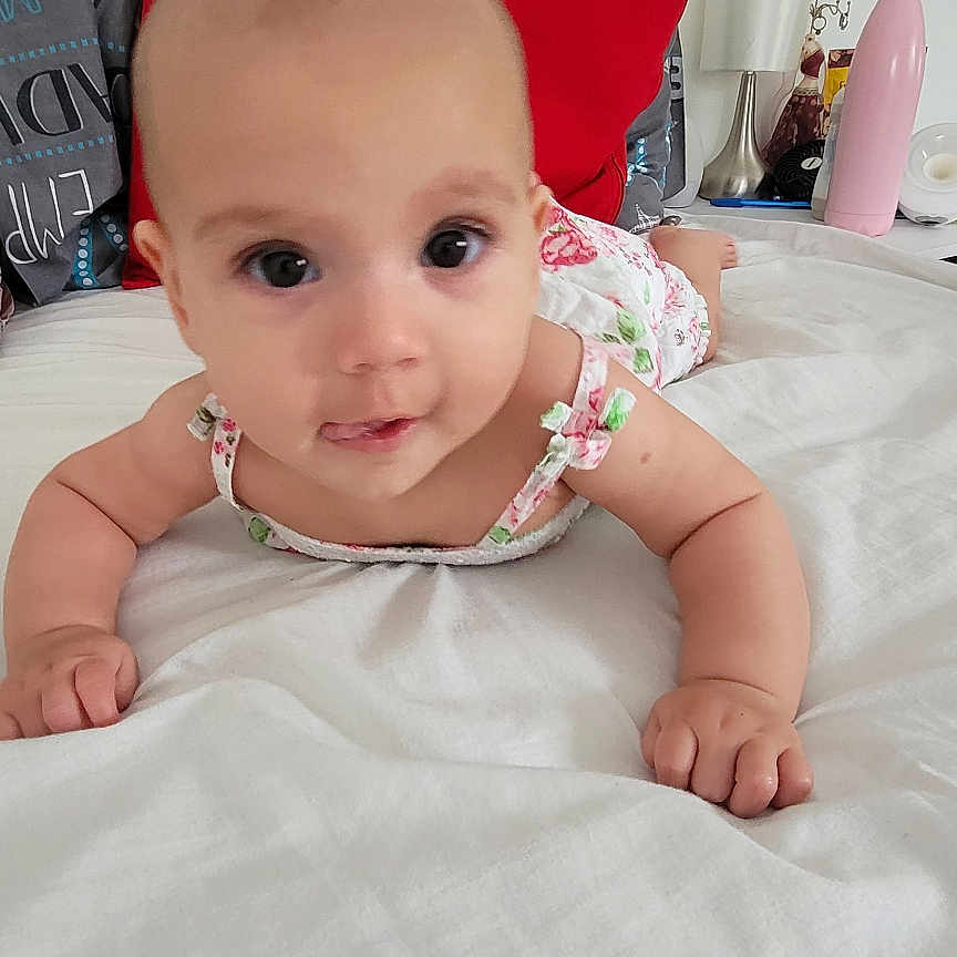 Sophia joined the competition — help win amazing prizes! arms, baby, bed, bedding, child, curious, cute, decor, face, furniture, home, indoor, infant, lamp, person, pillow, pink_bottle, sleepwear, smiling, white_bedspread