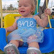 Octavia is registered to the contest to win money with this photo: baby, child, swing, outdoor, smiling, happy, blue_dress, footwear, grass, tree, toy, playground, person, cute, summer, nature, greenery, sunlight, toddler, fun