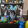 dog, bunny_ears, bandana, easter_eggs, basket, toy, holiday, decoration, living_room, wooden_floor, furniture, plush_toy, colorful, festive, indoors, pet, cute, celebration, spring, playful