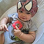 baby, child, helmet, spiderman, teether, gray_onesie, curly_hair, indoor, cushion, soft_bedding, cute, smiling, holding, infant, person, closeup, relaxed, toy, headgear, comfortable