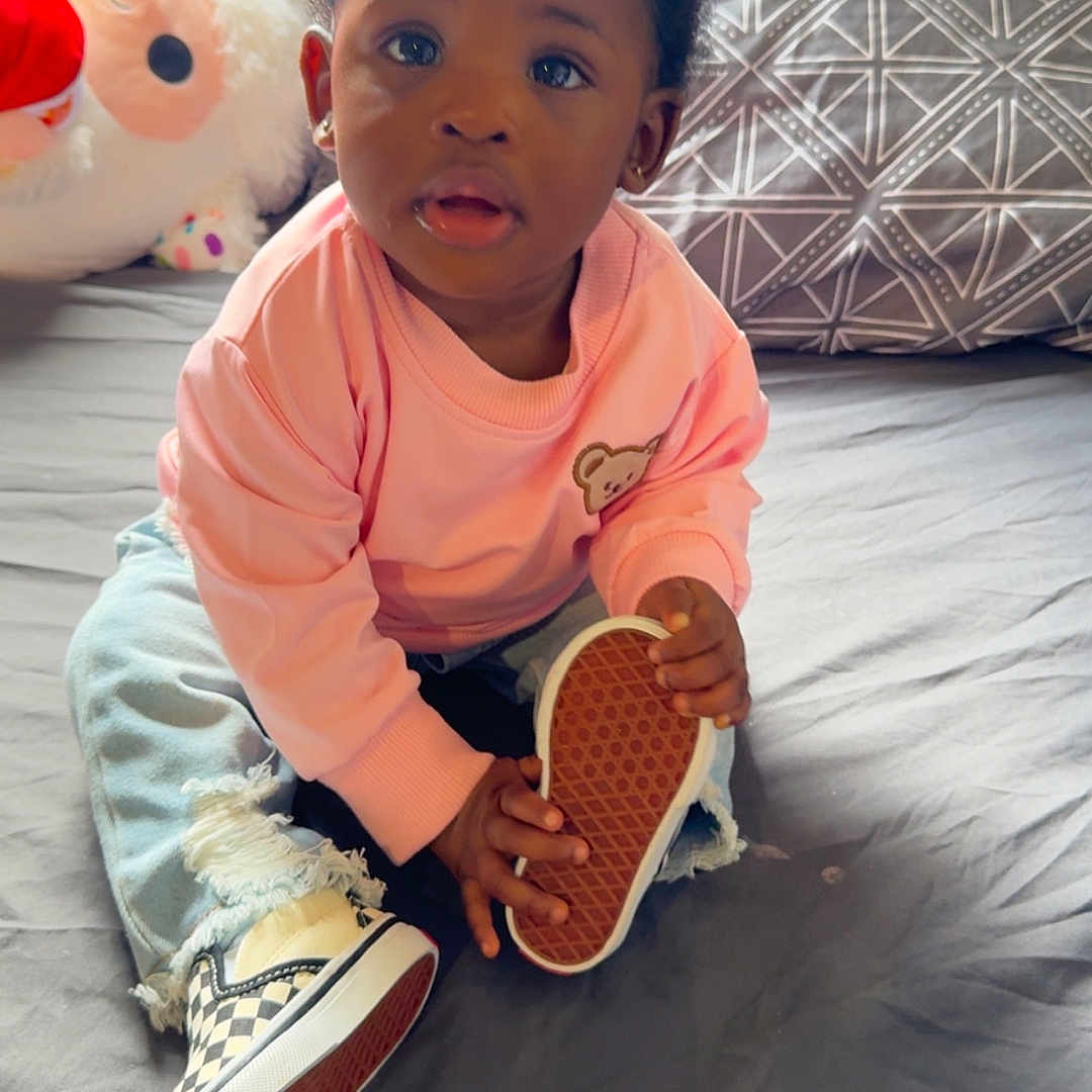 Ryla is registered to the contest to win money with this photo: bed, casual_clothing, child, curly_hair, cute, footwear, holding, home, indoor, person, pillow, pink_sweater, portrait, ripped_jeans, shoe, sitting, stuffed_animal, sunglasses, toddler, young_child
