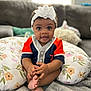 baby, infant, child, headband, flower, pillow, floral_pillow, couch, indoor, smiling, happy, cute, hands, feet, clothing, person, portrait, sitting, home, cozy