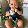 baby, infant, child, smiling, sitting, bouncer, baby_seat, plush_toy, toy, blue_shirt, bib, wristband, hands, fingers, portrait, indoors, playtime, colorful, happy, safety_label