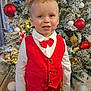 child, boy, red_vest, bow_tie, christmas_tree, ornaments, holiday, smiling, indoor, decorations, plush_toy, polar_bear, festive, happy, portrait, winter, celebration, white_shirt, floor, home