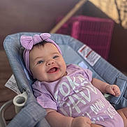 Mikiah joined the competition — help win amazing prizes! adorable, baby, baby_seat, blue_eyes, blurred_background, bow, cheeks, close_up, happy, headband, infant, onesie, portrait, print_on_clothing, purple_clothing, reclined, small_hands, smiling, soft_lighting, wooden_deck