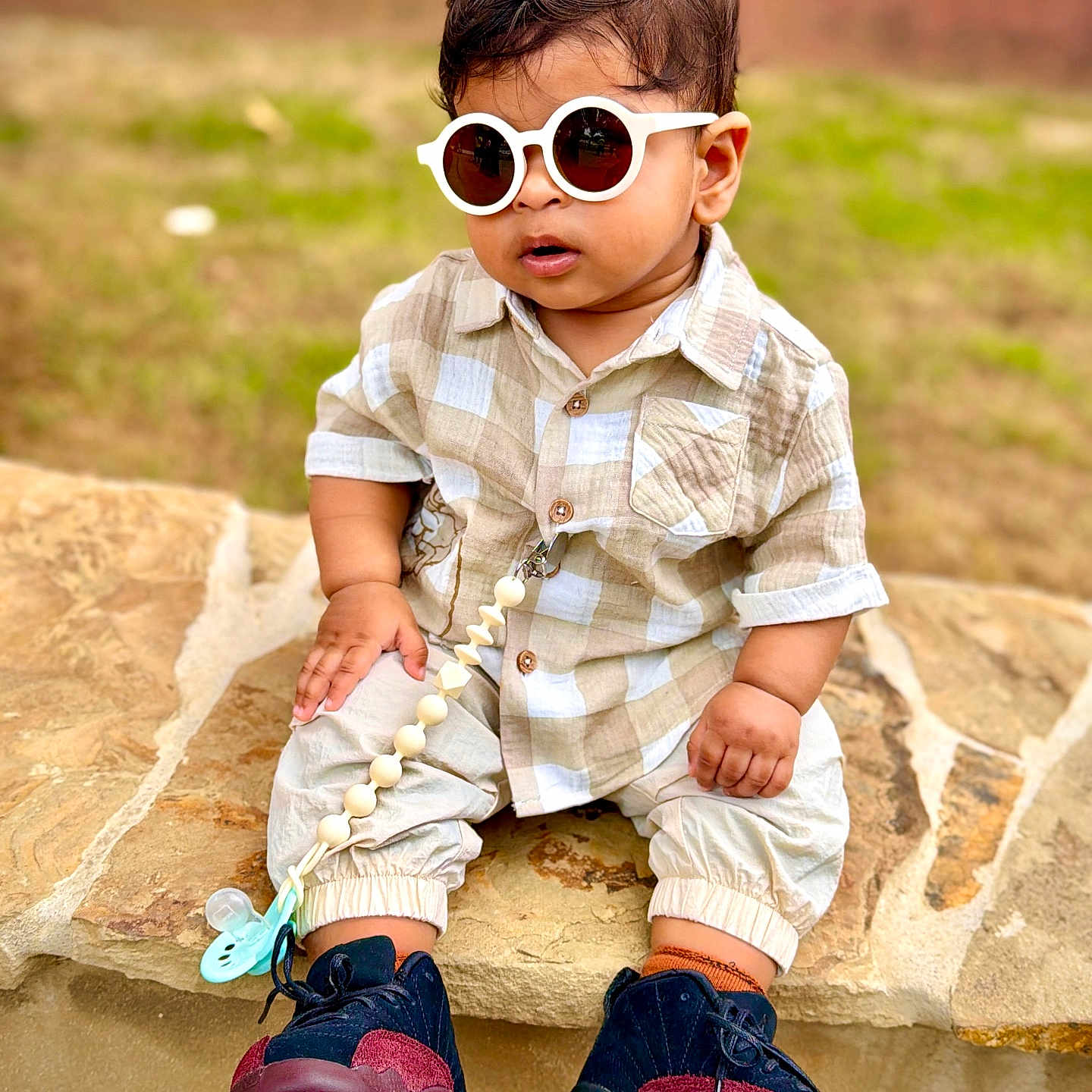 Adrian is registered to the contest to win money with this photo: toddler, child, sunglasses, shirt, pants, sneakers, stone, outdoor, grass, fashion, cute, baby, footwear, accessory, pacifier, casual, sitting, young_child, portrait, summer