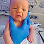 newborn, baby, gloved_hand, hospital, medical_equipment, crib, clipboard, bed, infant, person, skin, face, hand, clothing, healthcare, patient, medical, hospital_room, closeup, expression
