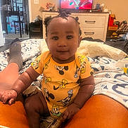 Azaan is registered to the contest to win money with this photo: baby, child, infant, sitting, smiling, portrait, indoors, bedroom, bed, blanket, pajamas, disney, mickey_mouse, orange_clothing, family, television, video_game, dresser, home, cozy