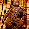 baby, blanket, brown_clothing, child, close_up, colorful, corduroy, cozy, face, feet, hands, indoor, infant, lying_down, mickey_mouse, overalls, plaid, portrait, tablet, toy