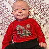 baby, infant, child, portrait, smiling, happy, sitting, lying_down, red_shirt, black_pants, clothing, blanket, patterned_blanket, indoors, close_up, face, eyes, head, construction_graphic, photography