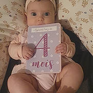 Esmée participe au concours pour gagner de l'argent avec cette photo : baby, child, infant, headband, milestone_card, pink_clothing, patterned_cushion, hands, feet, face, wide_eyes, lying_down, cute, indoor, portrait, close_up, soft_lighting, adorable, milestone, person