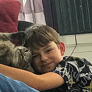 Topaze participe au concours pour gagner de l'argent avec cette photo : boy, child, cat, tabby_cat, cuddling, smiling, indoor, floor, tile_floor, red_cushion, curtains, casual_clothing, short_hair, pet, affection, friendship, relaxing, cozy, comfort, happy