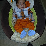 Mustafa is registered to the contest to win money with this photo: baby, child, infant, plaid_shirt, orange_pants, blue_socks, baby_seat, cushion, floor, tile_floor, footwear, shoe, person, indoor, expression, curious, confused, clothing, furniture, portrait