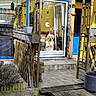 dog, golden_retriever, glass_door, blue_door_frame, yellow_wall, wooden_structure, garden, potted_plant, patio, tiles, sunlight, outdoor, fence, reflection, house, door_handle, bench, plants, wood, cozy